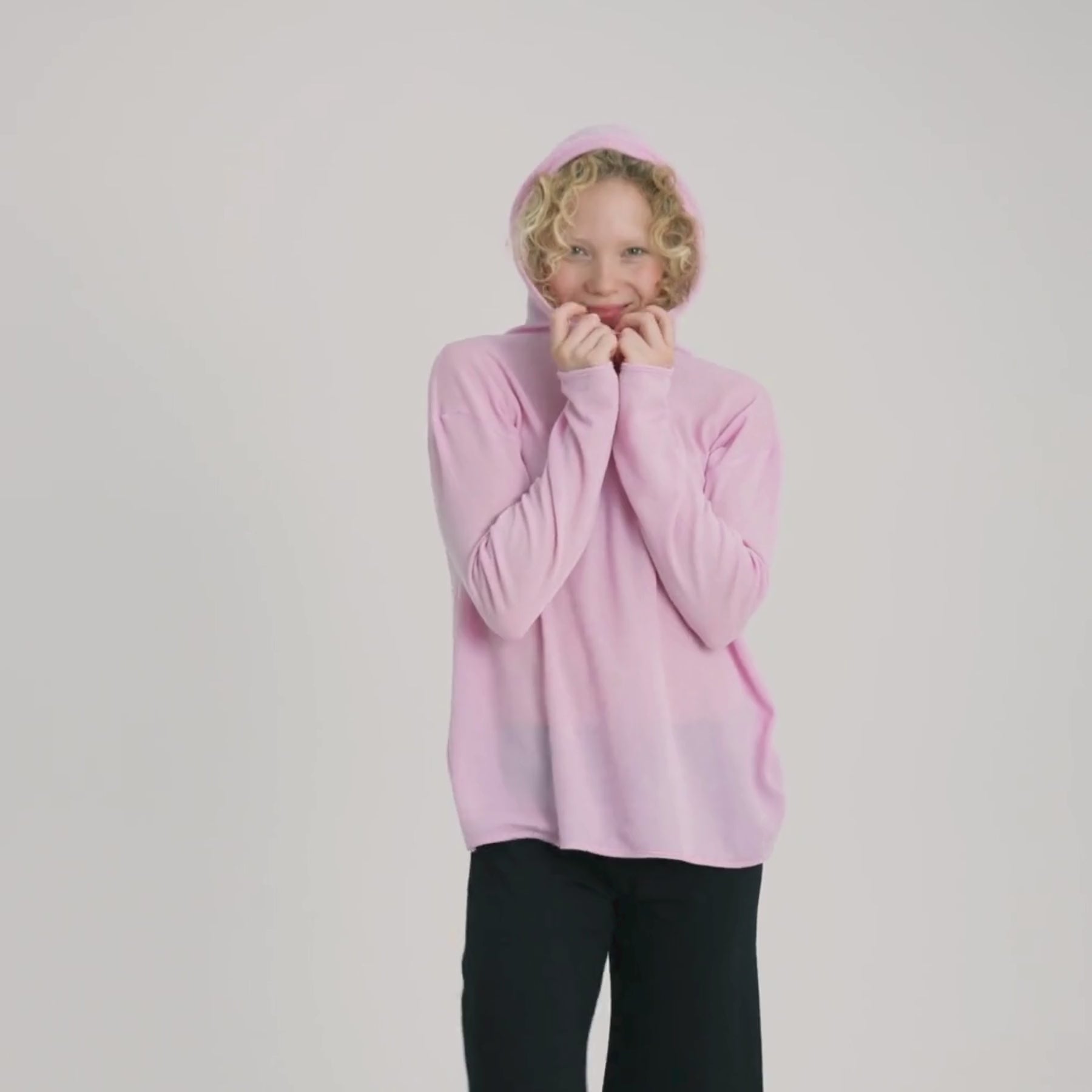 Ylellisen pehmeä vaaleanpunainen merinosilkkihuppari videolla. Malli laittaa hupun päähän ja ihastelee pehmeyttä.