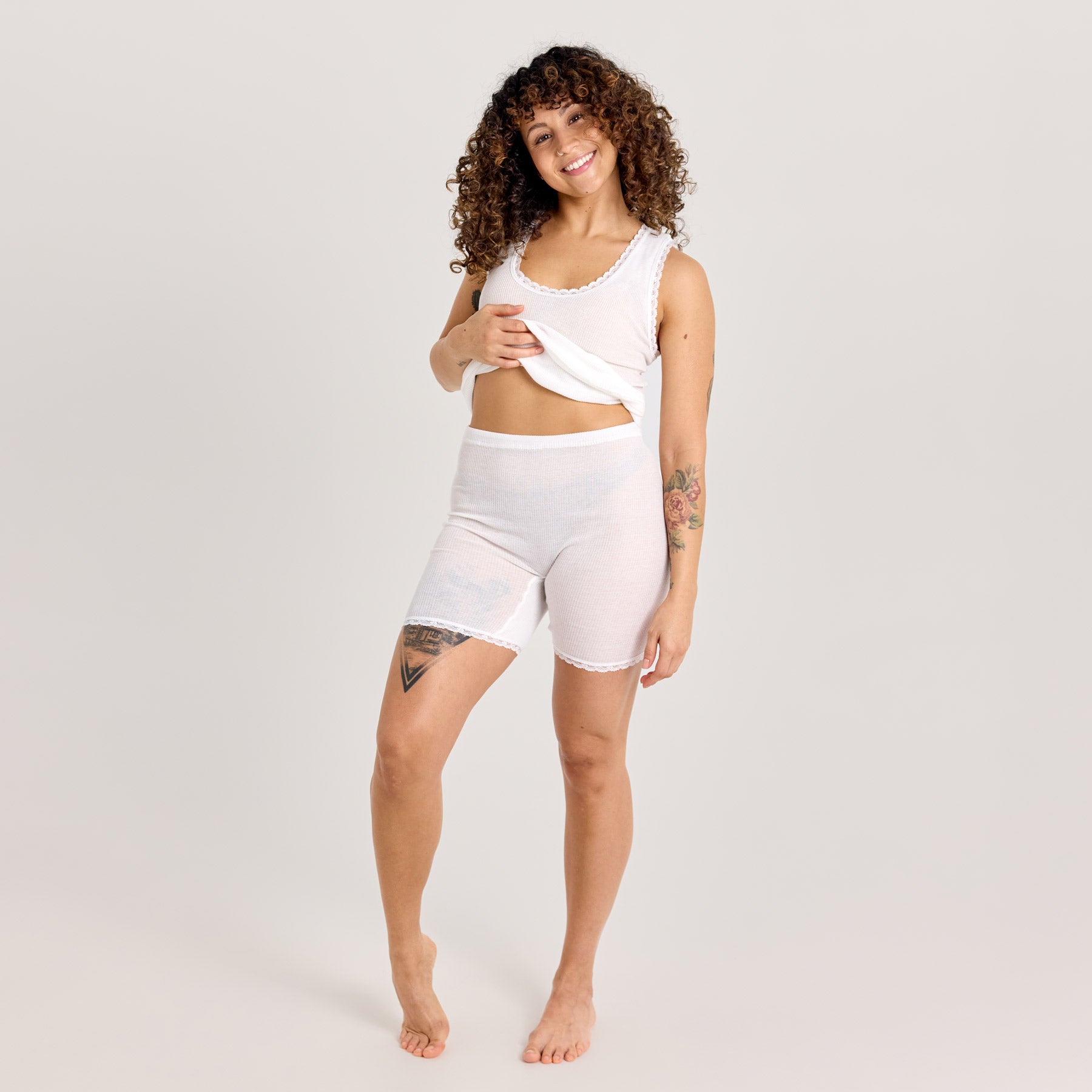 Valkoiset naisten laama lahjehousut ja valkoinen hihaton laamapaita kuvassa. Malli nostaa hieman paitaa, jolloin lahjehousujen vyötärö tulee esille.