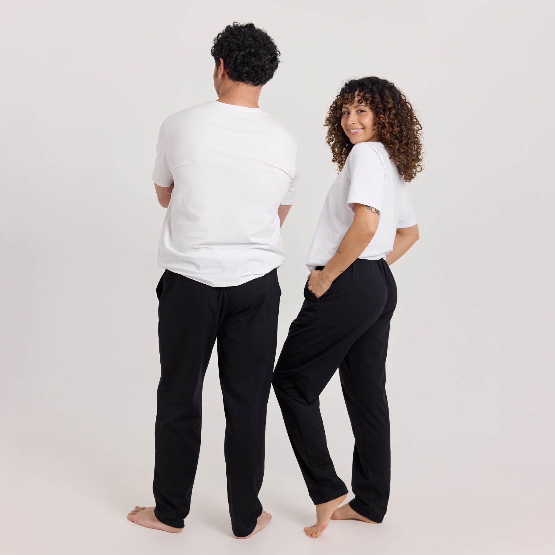 Jokapaikan housut mustana naisella ja miehellä, yhdistettynä valkoiseen t-paitaan. Tyylikkäät ja kevyet housut työ- ja vapaa-aikaan.