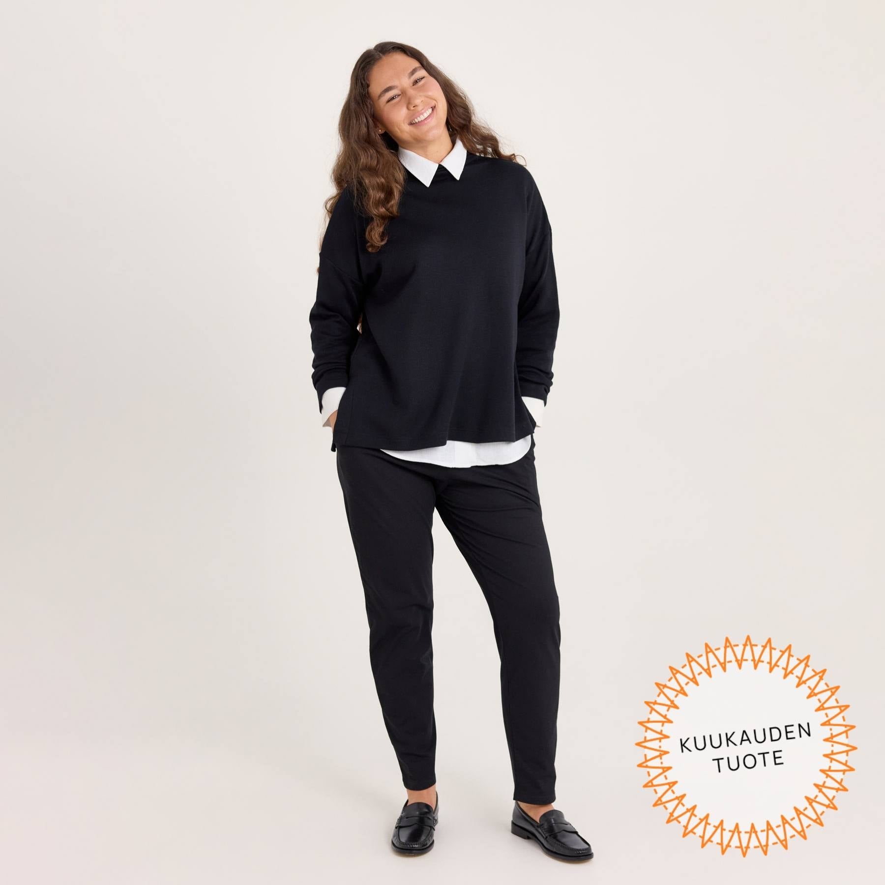 Mustat Jokapaikan housut kuvattuna edestä päin. Mallilla on kädet taskuissa.