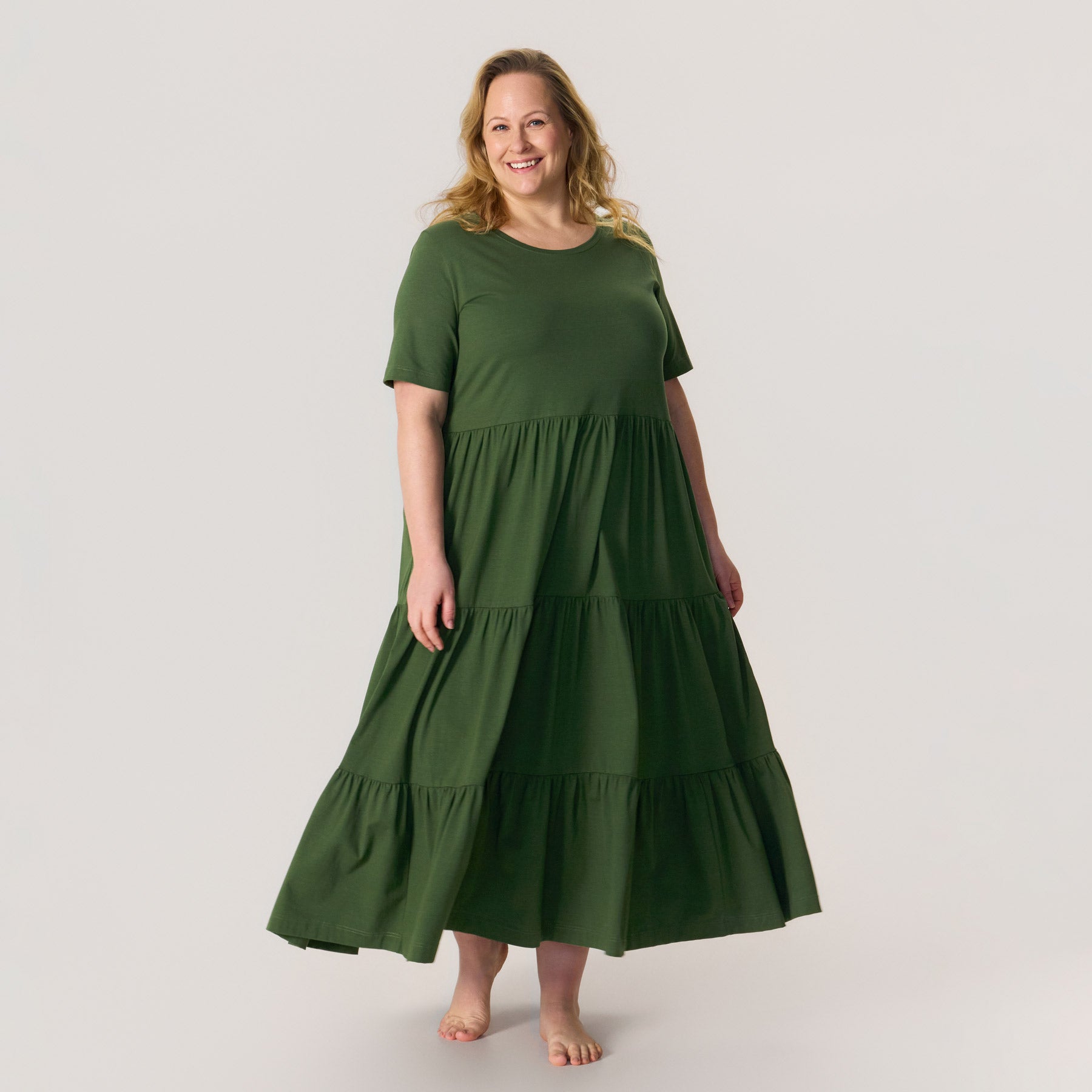 Maxi-pituinen frillamekko maastonvihreänä. Mekossa on taskut ja pyöreä pääntie. Valmistettu Suomessa, Kangasalla.
