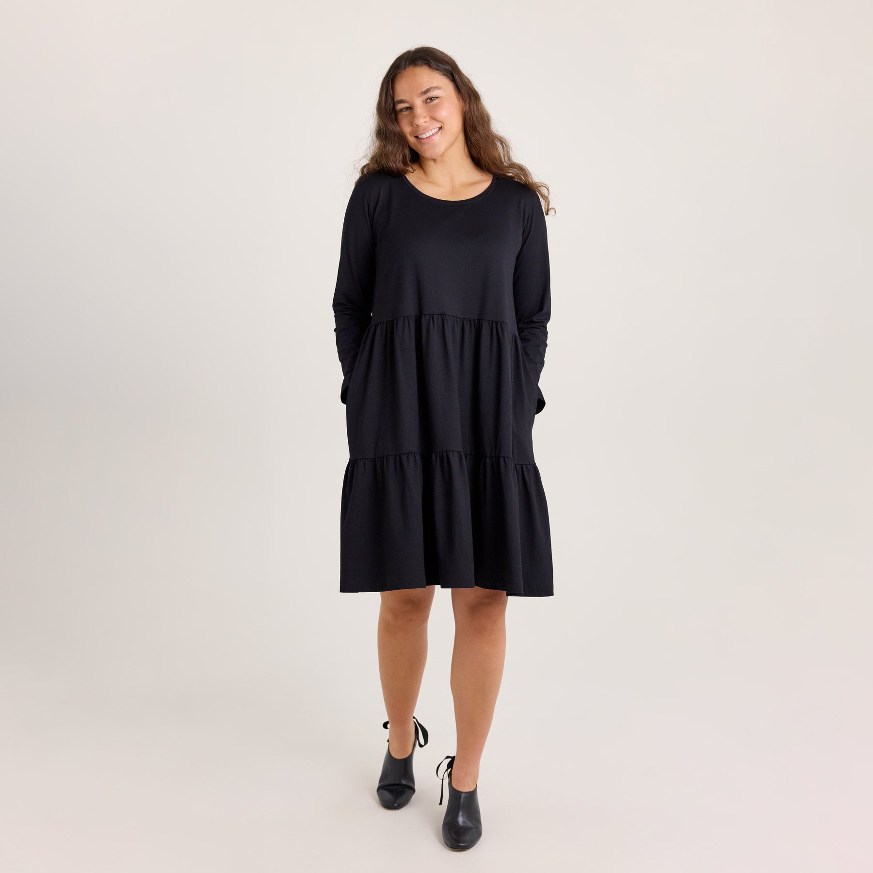 Mallilla on päällä mustan värinen frillamekko. Malli pitää käsiään taskuissa.