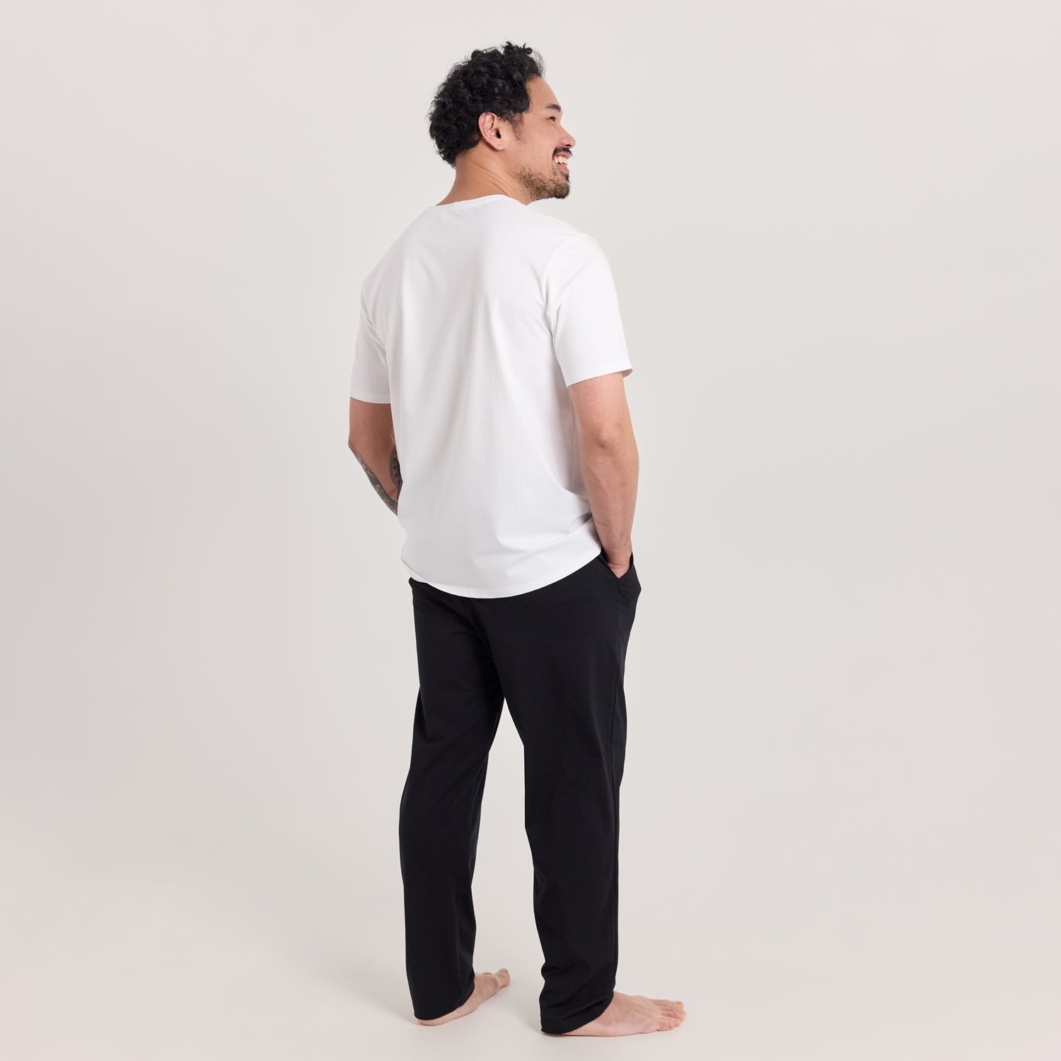 Mies takaa päin pukeutuneina valkoiseen t-paitaan ja mustiin Jokapaikan housuihin, jotka ovat unisex-malliset. Monikäyttöiset housut arkeen ja vapaa-aikaan.