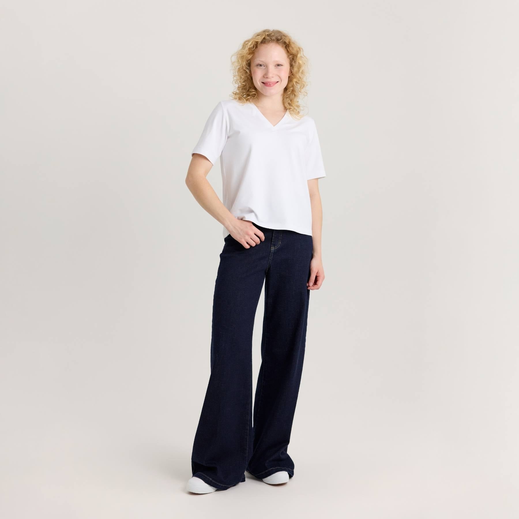 Mallilla on päällä valkoinen Jokapaikan t-paita ja tummansiniset leveälahkeiset farkut.