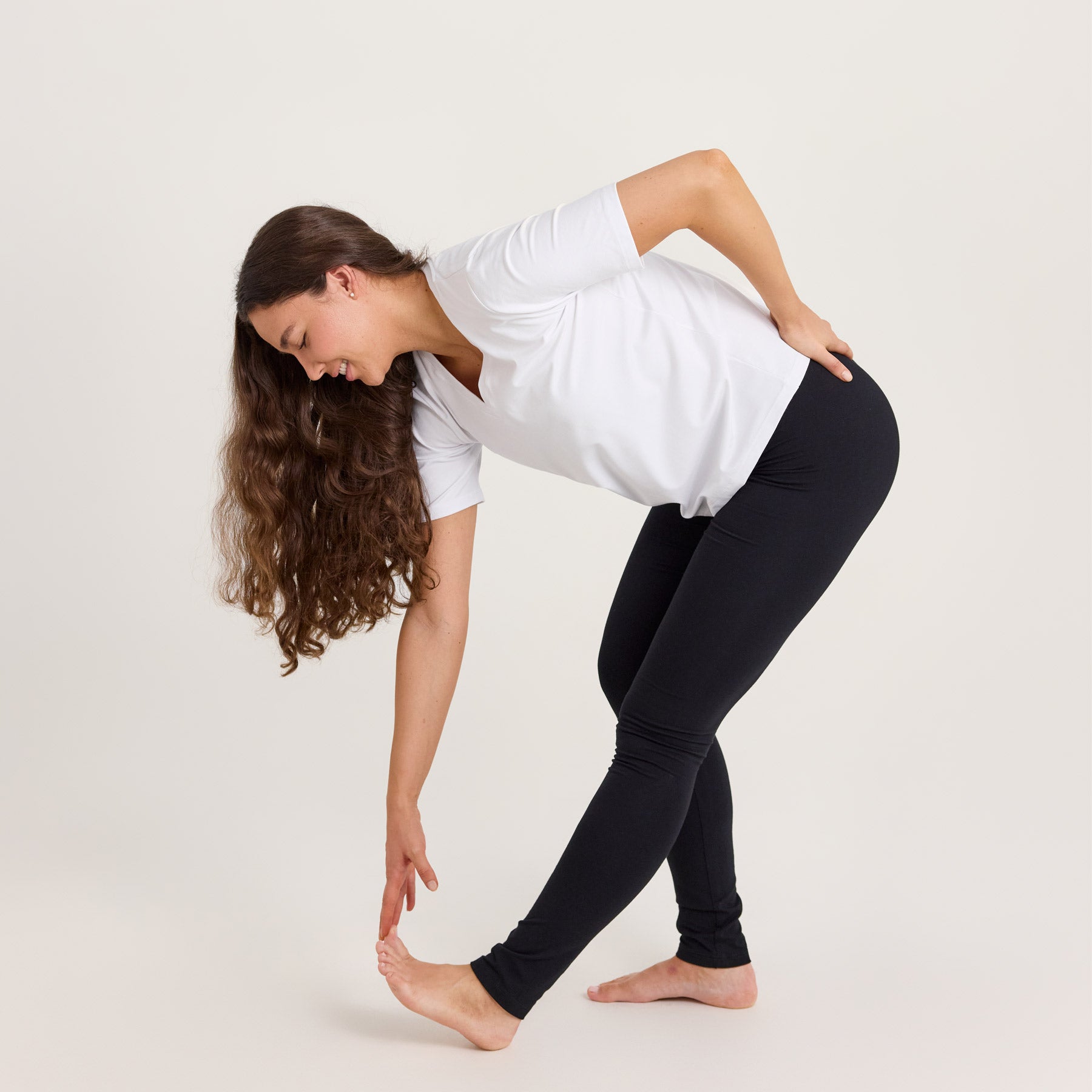 Mallilla on mustat bambuleggingsit ja valkoinen Jokapaikan t-paita. Hän koskettaa toisella kädellään varpaitaan venytysasennossa, mikä korostaa leggingsien sopivuutta myös urheiluun.