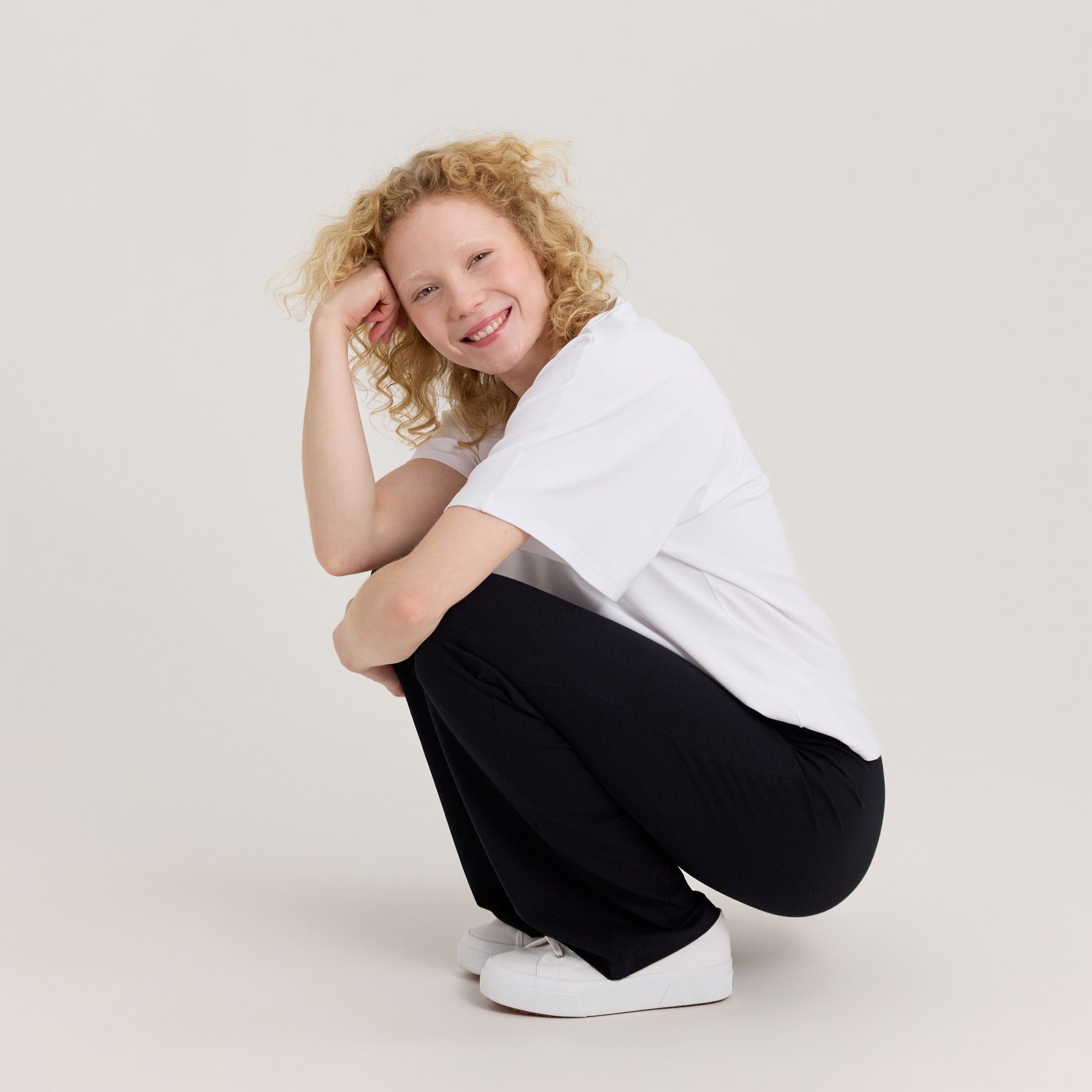 Malli kyykkyasennossa suorien bambuhousujen kanssa. Korkeavyötärö ja joustava istuvuus korostuvat.