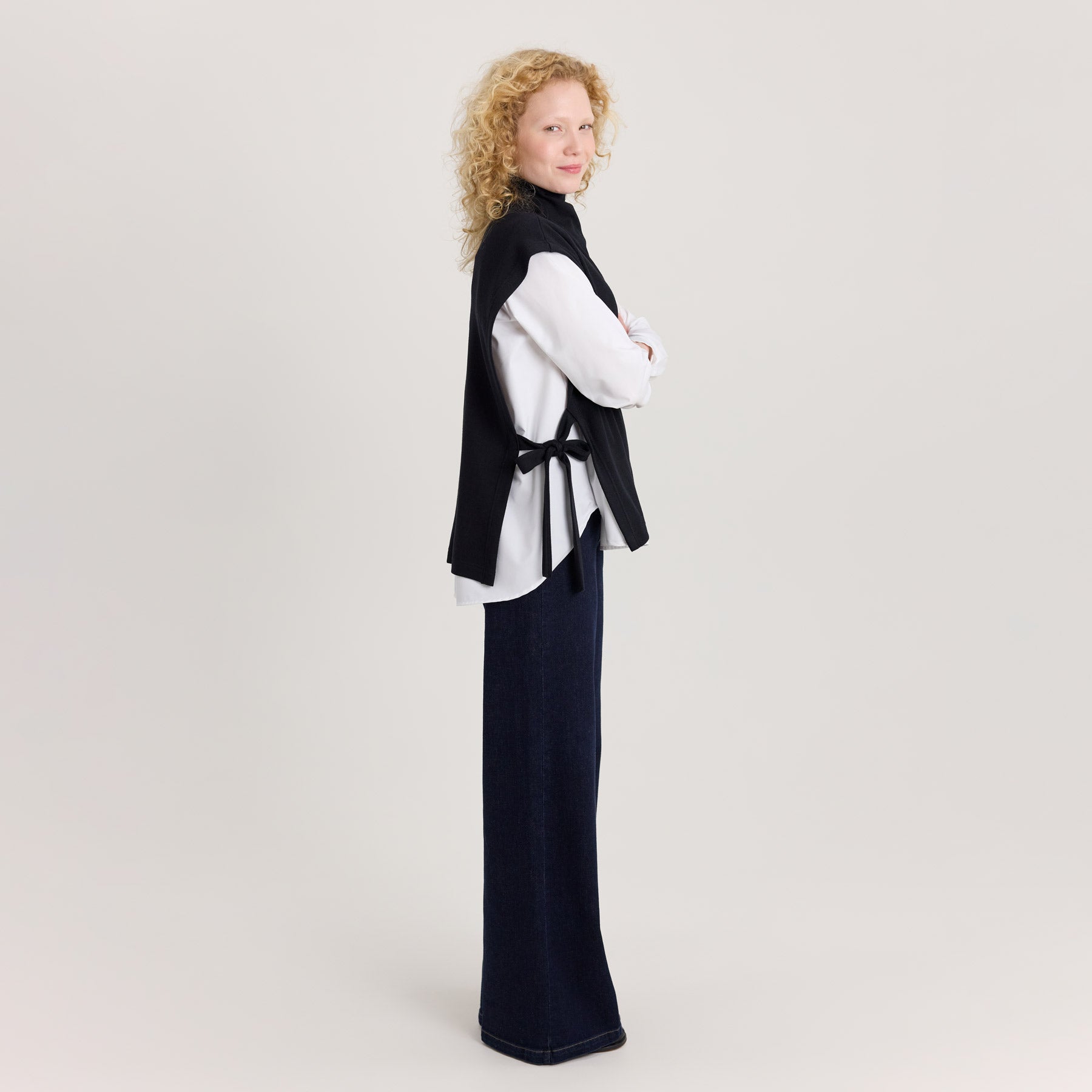 Mustan värinen neuleliivi. Suora malli, sivunauholla säädettävä istuvuus. Malli on puettu valkoiseen kauluspaitaan, jonka päällä on musta neuleliivi.