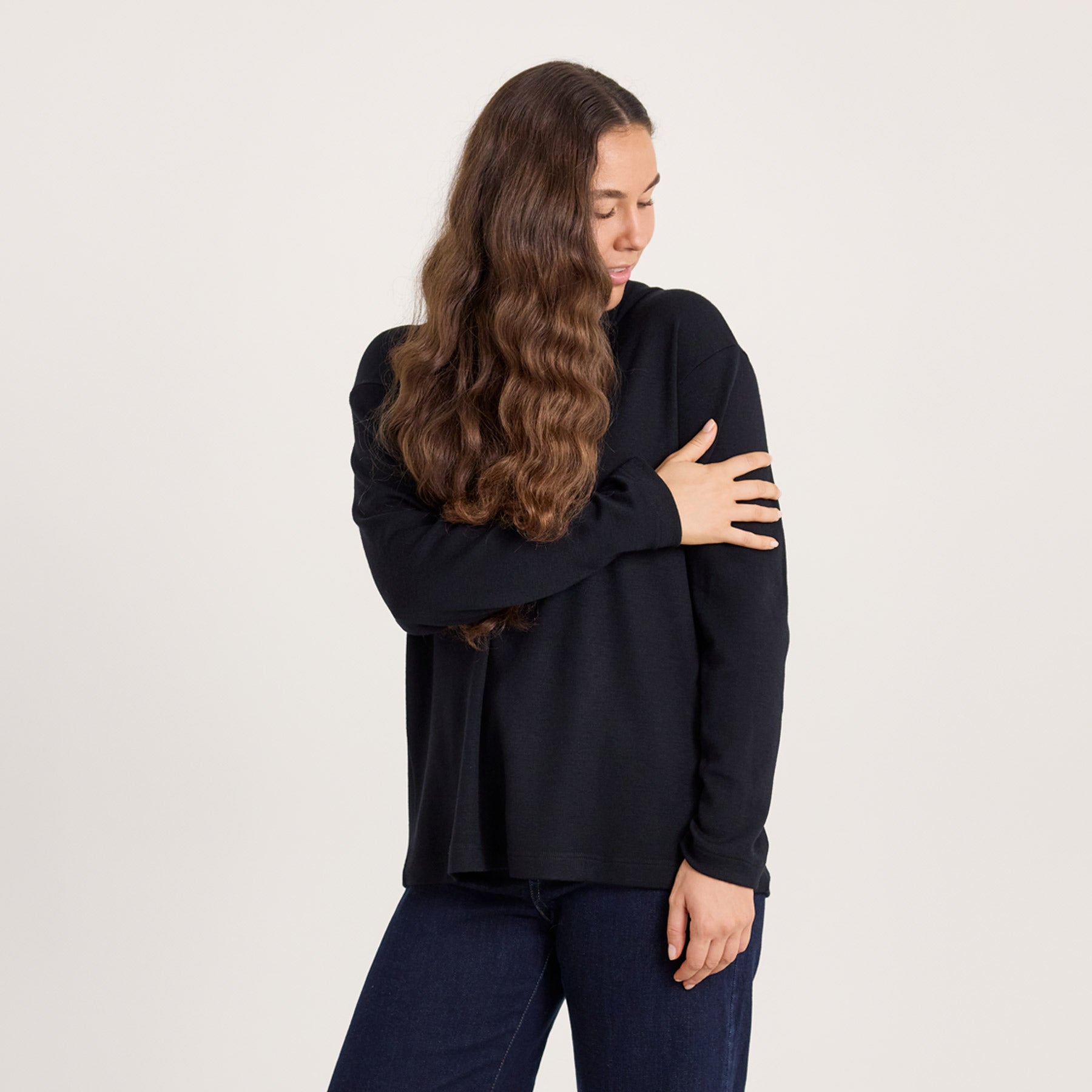 Kuvassa malli pitää toista kättä käsivarren päällä, ja tunnustelee pehmeää materiaalia. 100% merinovilla on pehmeä ja kutittamaton materiaali.