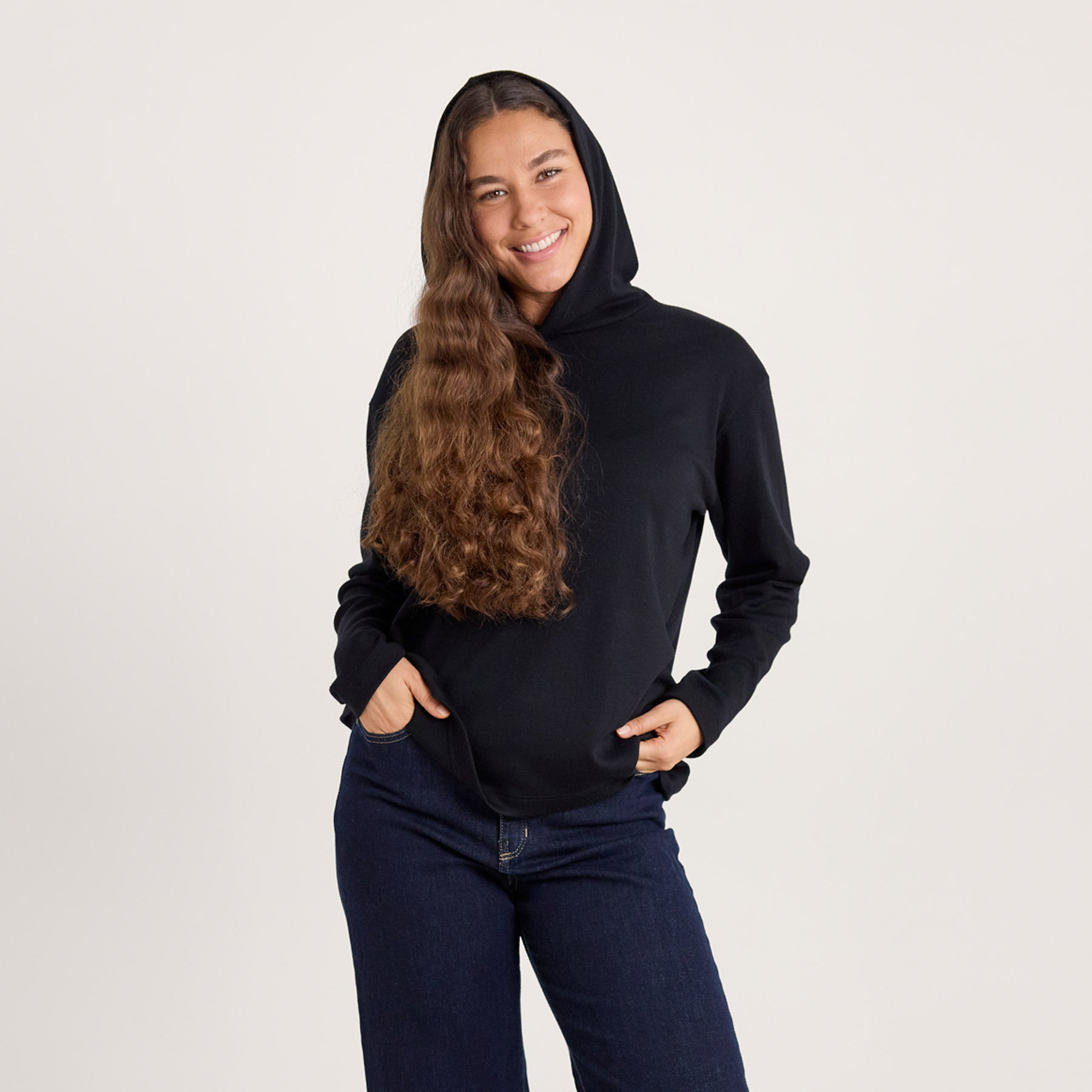 Lähikuvassa musta suora huppari. Mallilla on huppu päässä, ja huppu istuu kauniisti päähän.