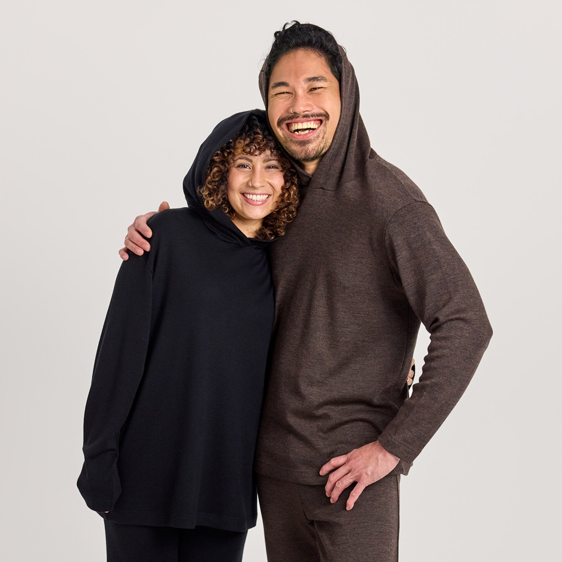 Naisella on päällä musta suora huppari ja miehellä meleerattu ruskea huppari. Mukava 100% merinovillainen unisex-mallinen huppari kaikille.