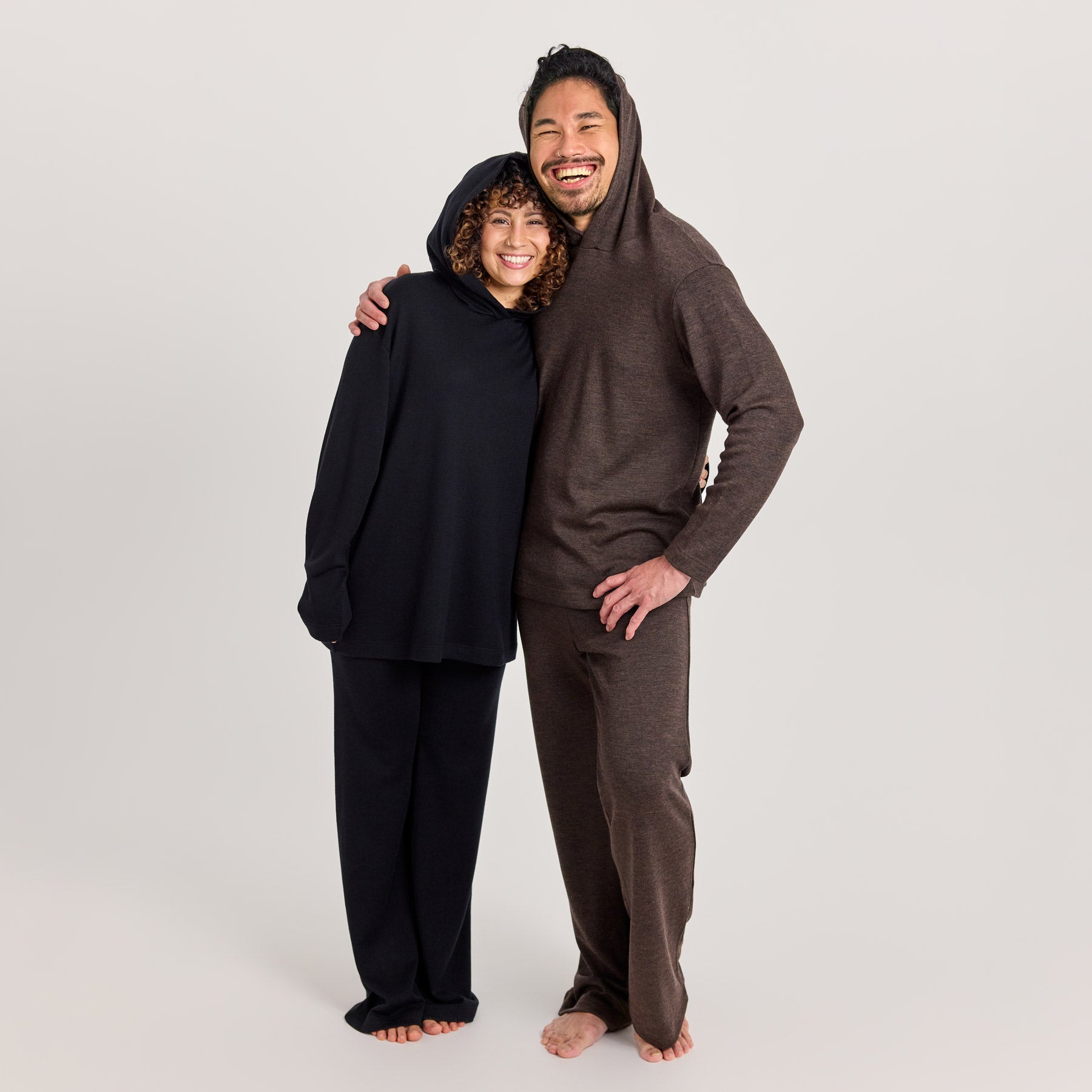 Naisella on päällä musta suora huppari ja rennot neulehousut. Miehellä on päällä meleeratun ruskea suora huppari ja rennot neulehousut. Valmistettu Suomessa.