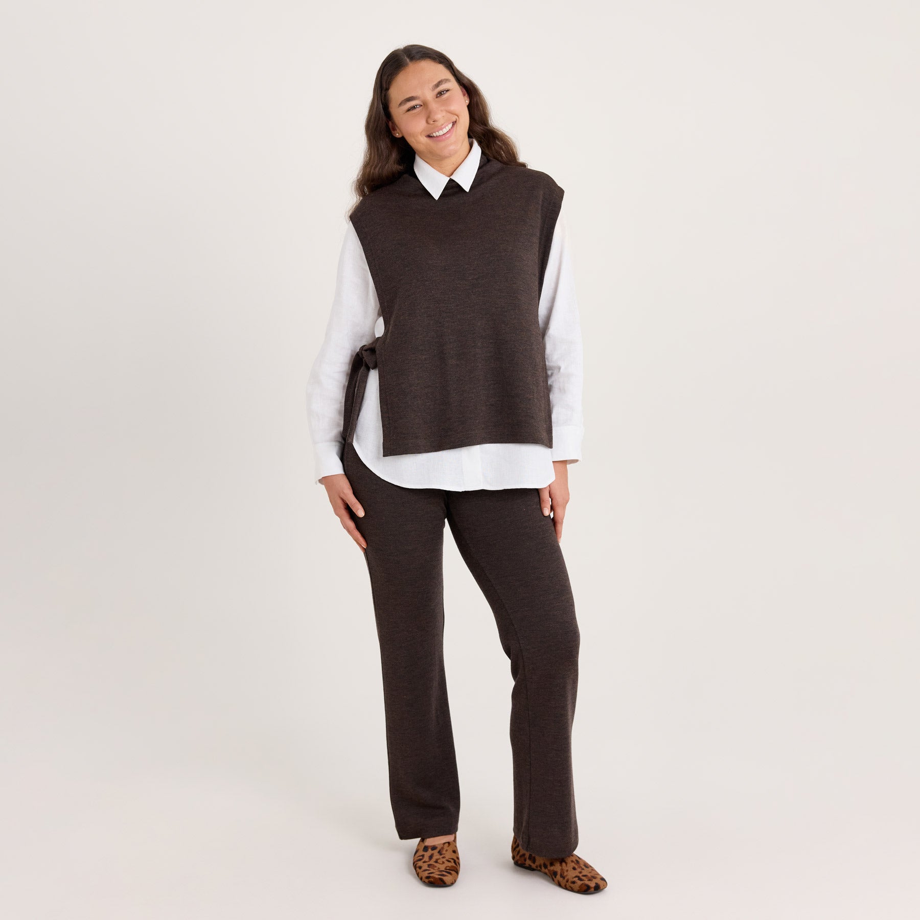 Liivikauluri ja rennot neulehousut pehmeässä meleeratun ruskeassa värissä. Liivikaulurin alla on valkoinen kauluspaita.