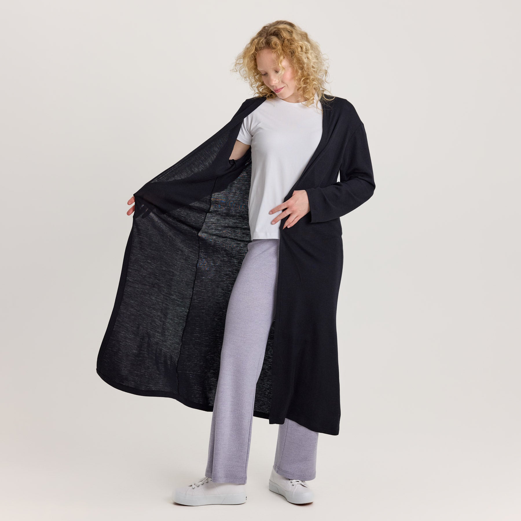 Malli avaa mustaa KAIHO pitkää neuletakkia sivulle. Tuoden sen kevyen, ohuen ja laskeutuvan merinosilkkimateriaalin esille.