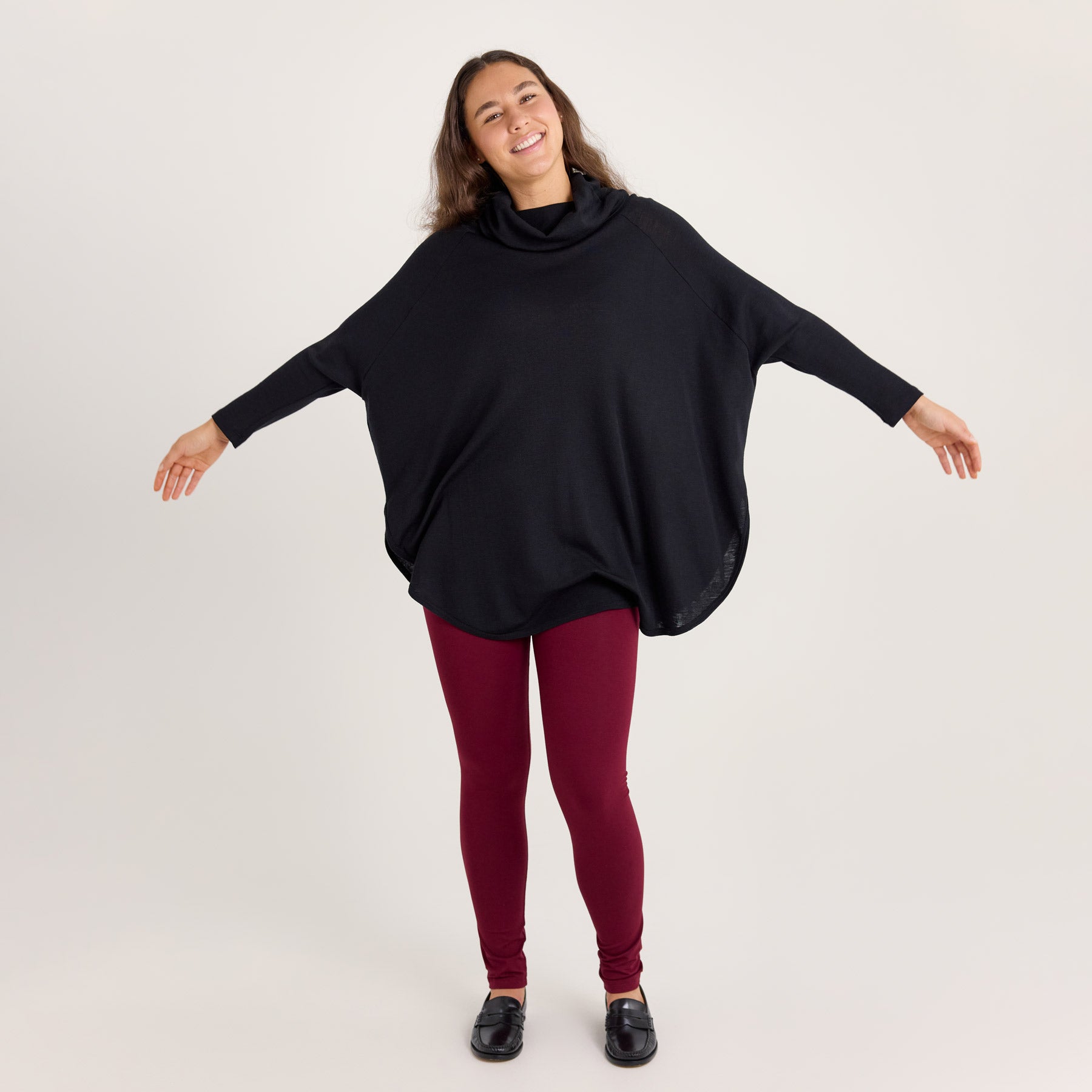 Malli levittää käsiään sivulle esitellen neuletunikan pyöreän ja väljän mallin. Neuletunikassa on kapeat hihat sekä halkiot molemmilla sivuilla.