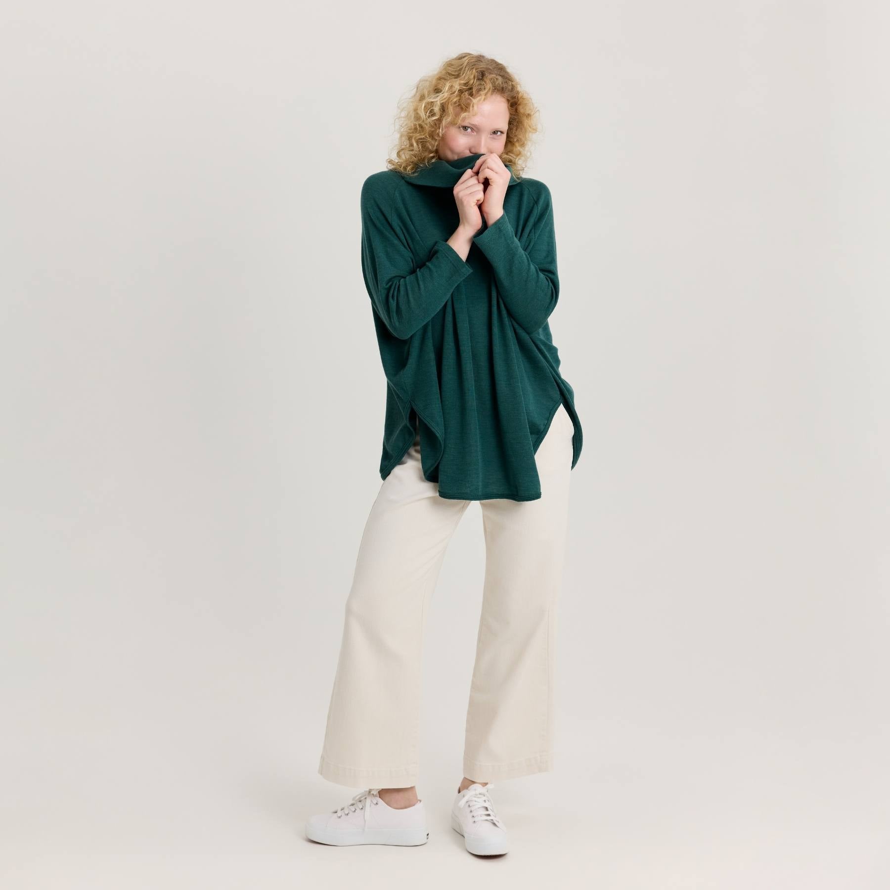 Vihreä neuletunika ja valkoset farkut. Neuletunika on valmistettu Kangasalla, Suomessa.