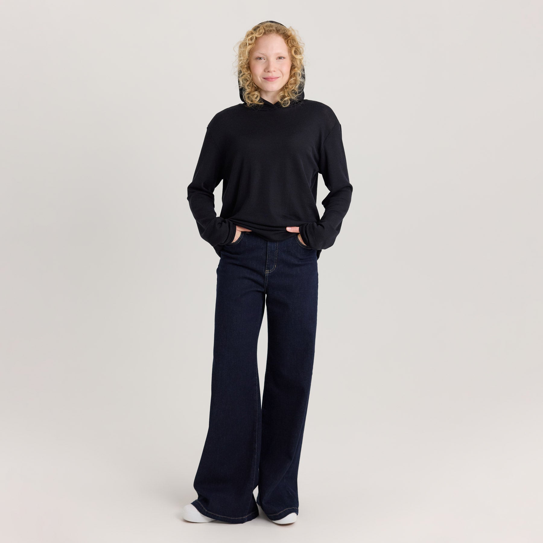 Mustan värinen unisex huppari yhdistettynä tummansinisiin leveälahkeisiin farkkuihin.