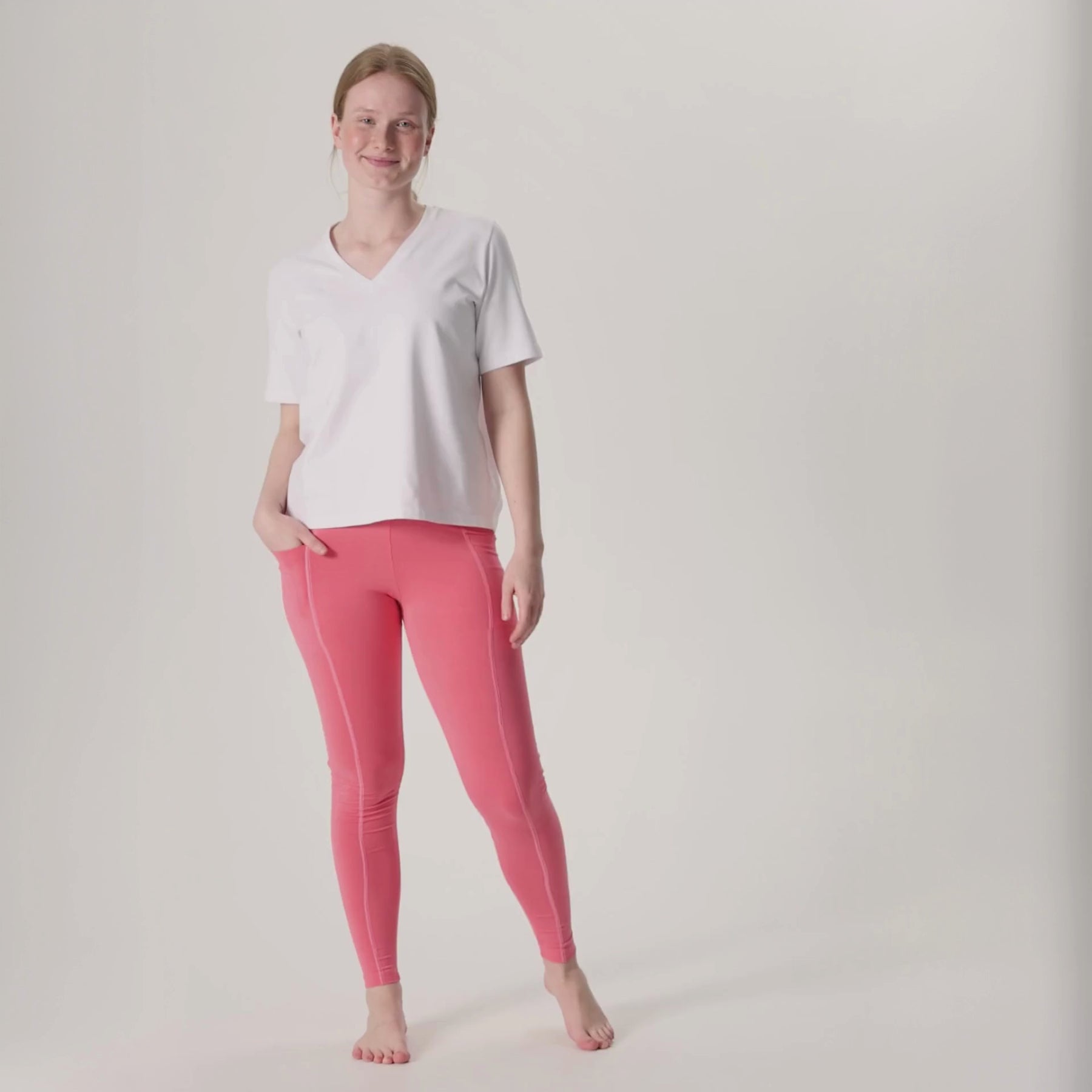 Videolla on korallipinkit LEMPI treenileggingsit ja valkoinen Jokapaikan t-paita. Mallilla on toinen käsi treenileggingsien reisitaskussa.