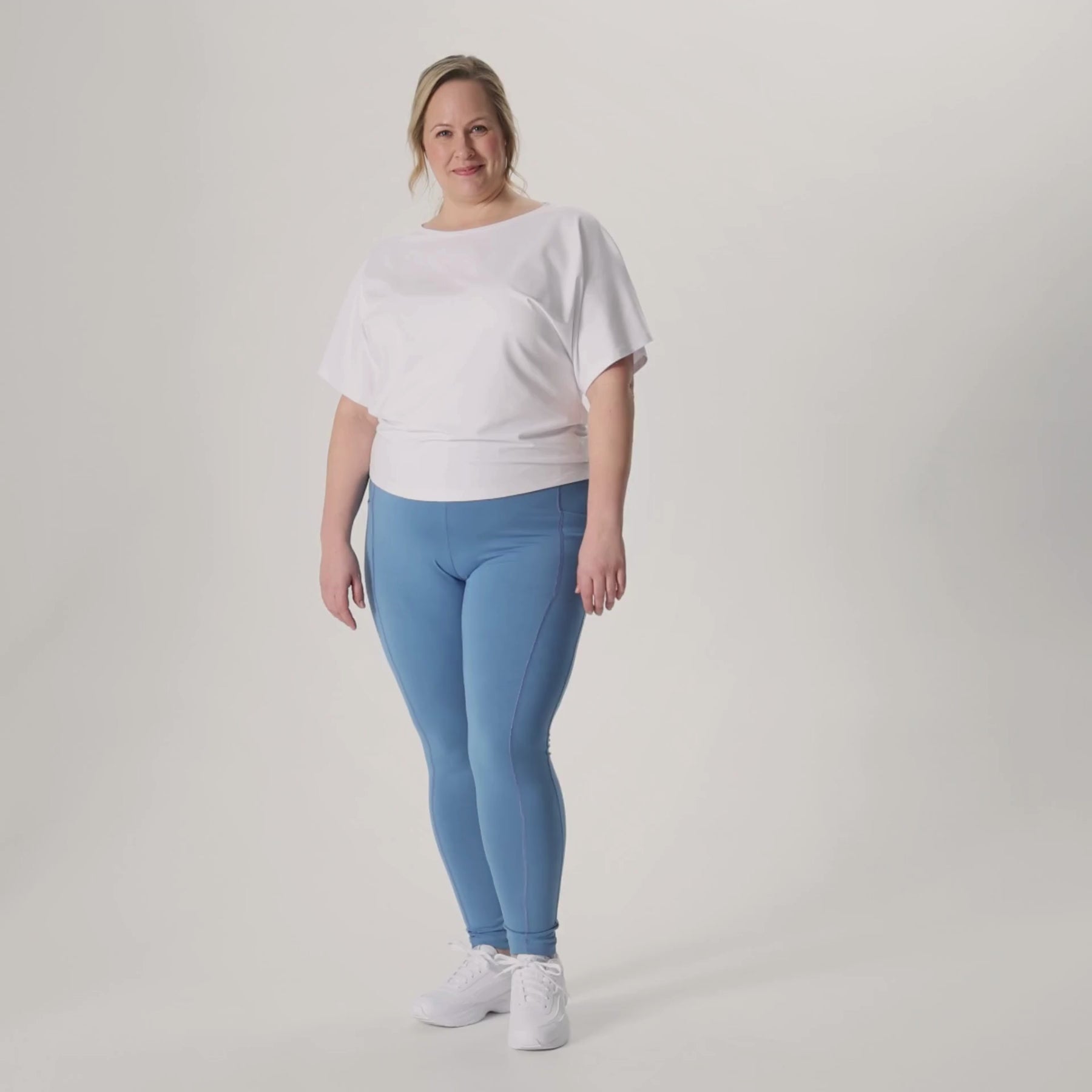 Harmaansiniset LEMPI treenileggingsit ja valkoinen Jokapaikan pusero. Malli näyttää videolla treenileggiensien kätevän reisitaskun.