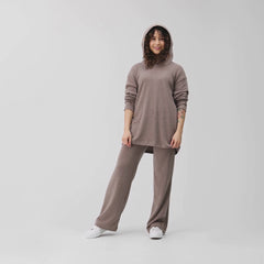 Videolla on suora huppari ja rennot neulehousut värissä meleerattu beige. Mallilla on hupparin huppu päässä,