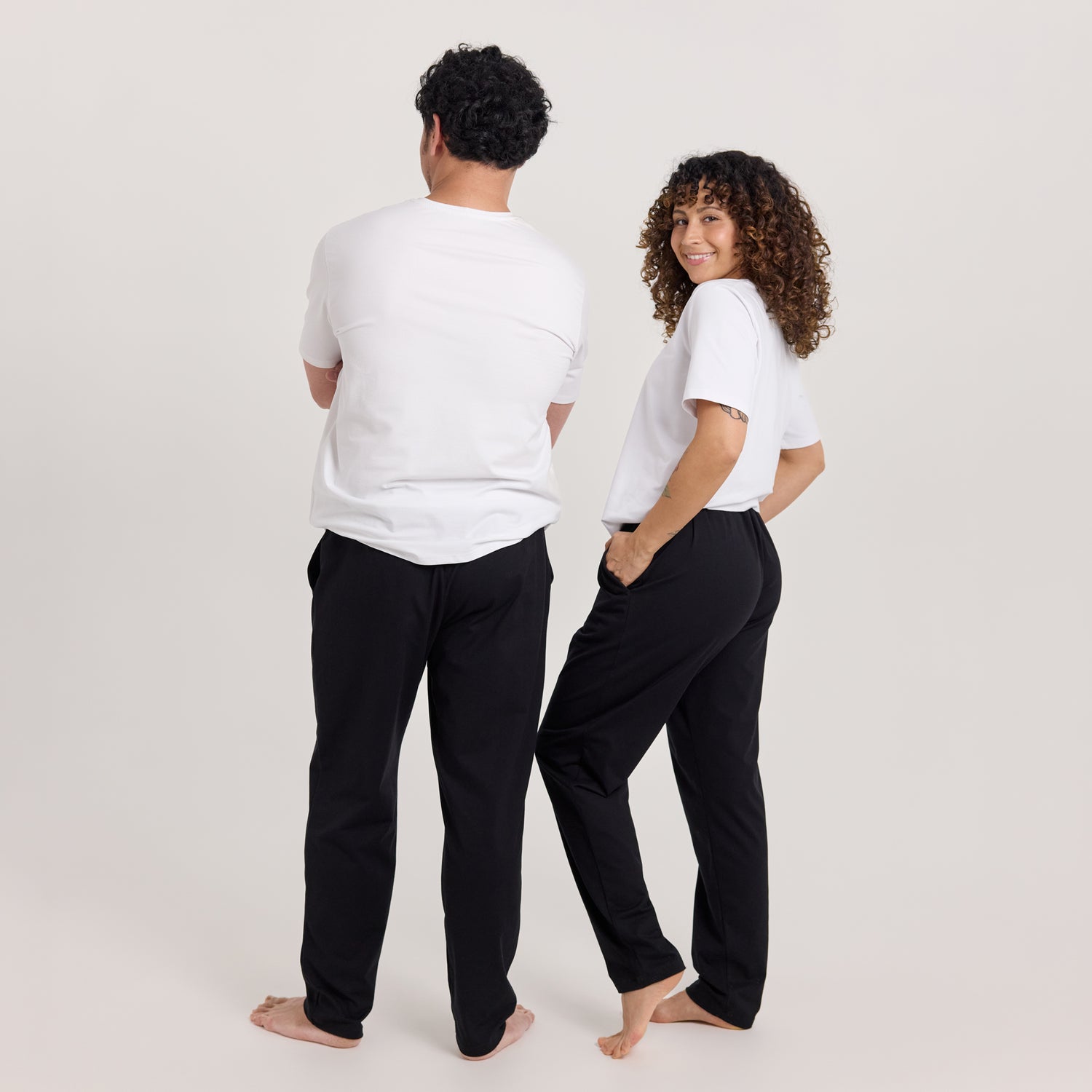Jokapaikan housut mustana naisella ja miehellä, yhdistettynä valkoiseen t-paitaan. Tyylikkäät ja kevyet housut työ- ja vapaa-aikaan.