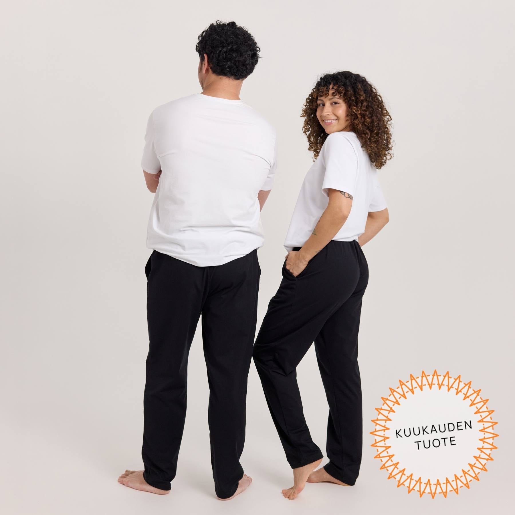 Unisex-malliset Jokapaikan housut kuvattuna miehen ja naisen päällä sivuttain, jolloin housut näkyvät takaapäin.
