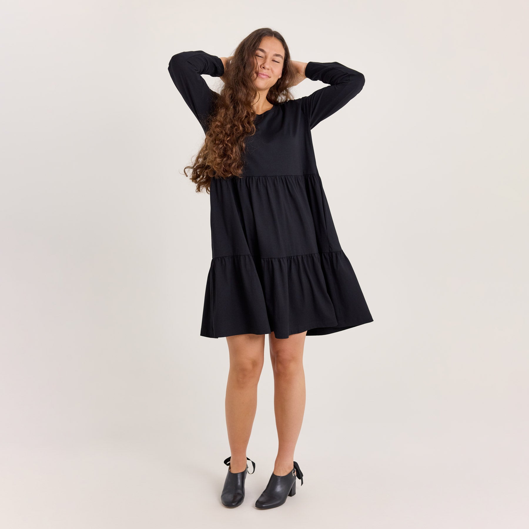 Midipituinen frillamekko värissä musta. Malli heilauttaa helmaa niin, että helman hulmuavaisuus tulee ilmi.