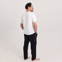 Mies takaa päin pukeutuneina valkoiseen t-paitaan ja mustiin Jokapaikan housuihin, jotka ovat unisex-malliset. Monikäyttöiset housut arkeen ja vapaa-aikaan.