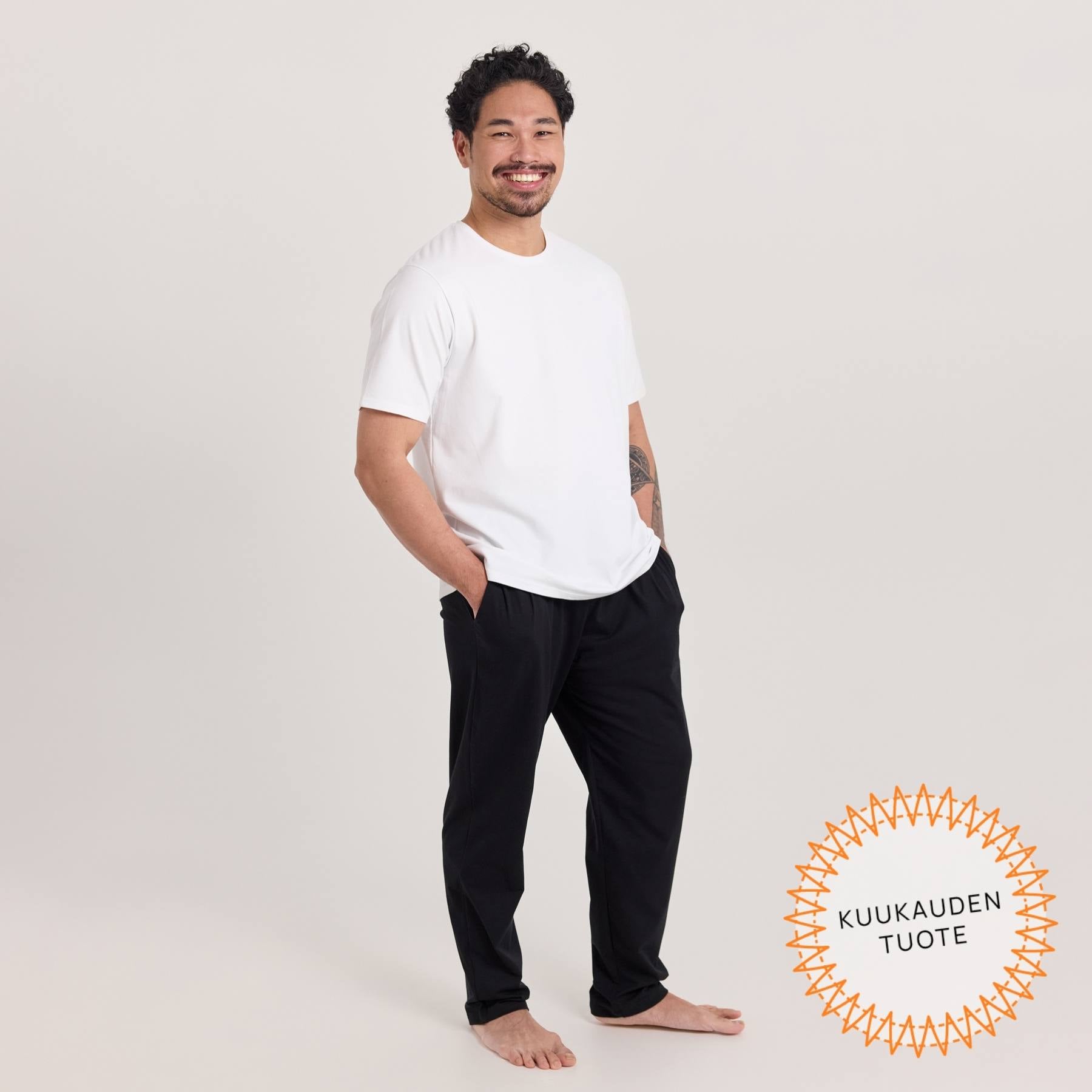 Mustat Jokapaikan housut ja valkoinen unisex t-paita miehen päällä.