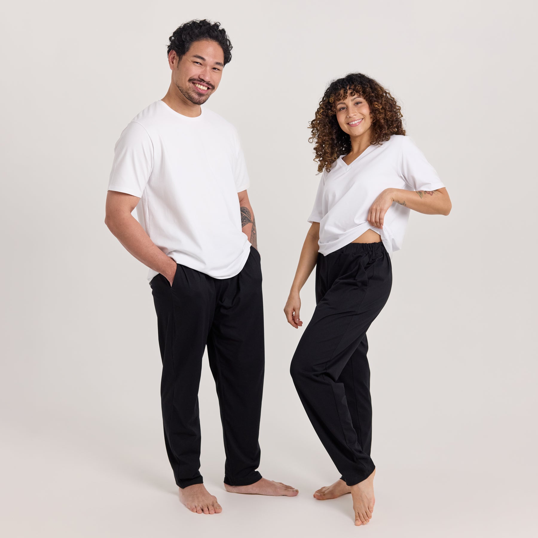 Nainen ja mies pukeutuneina valkoisiin t-paitoihin ja mustiin Jokapaikan housuihin, jotka ovat unisex-malliset. Monikäyttöiset housut arkeen ja vapaa-aikaan.