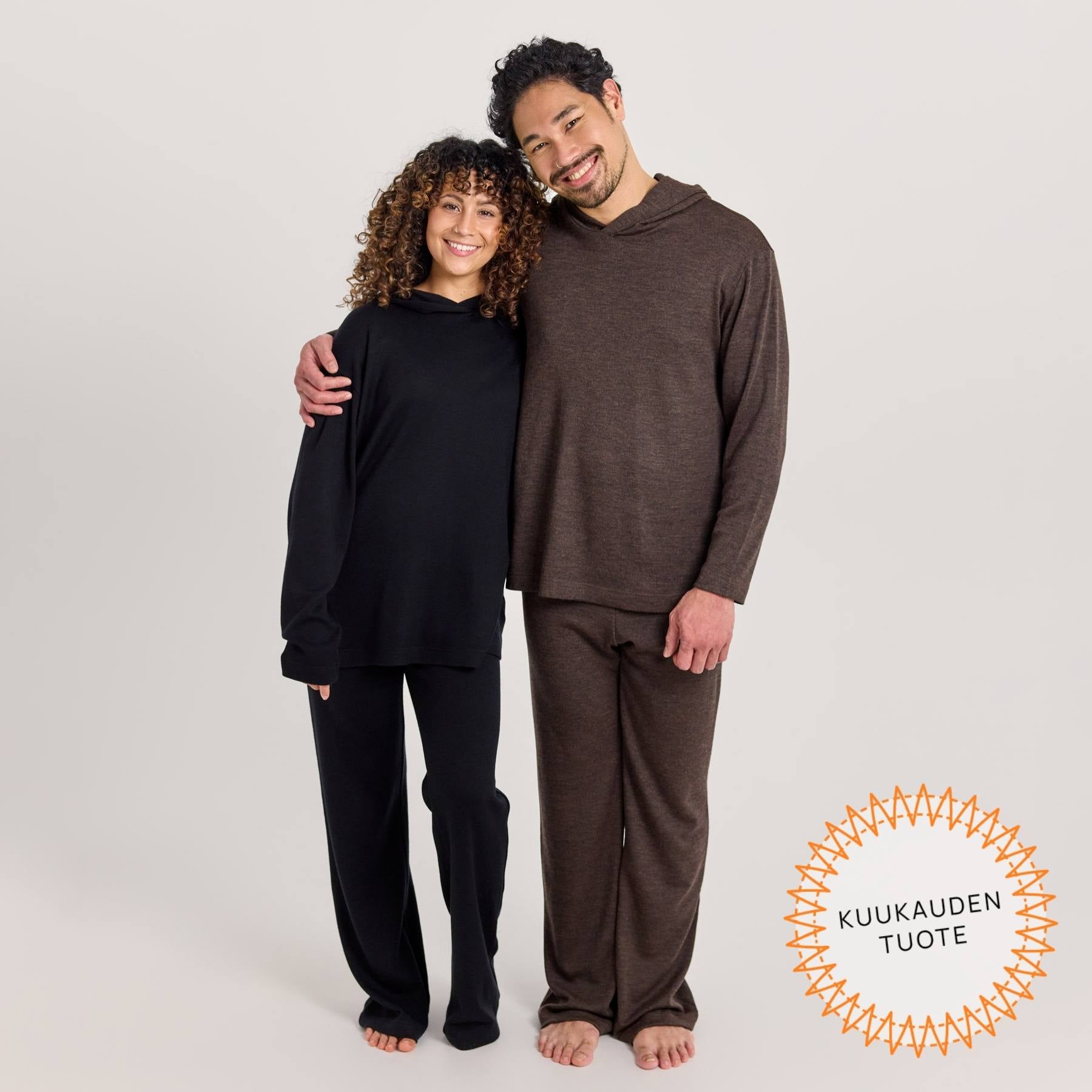 Kuvassa on nainen pukeutuneena mustiin rentoihin neulehousuihin ja suoraan huppariin. Miehellä on päällä meleeratut ruskeat rennot neulehousut ja suora huppari.