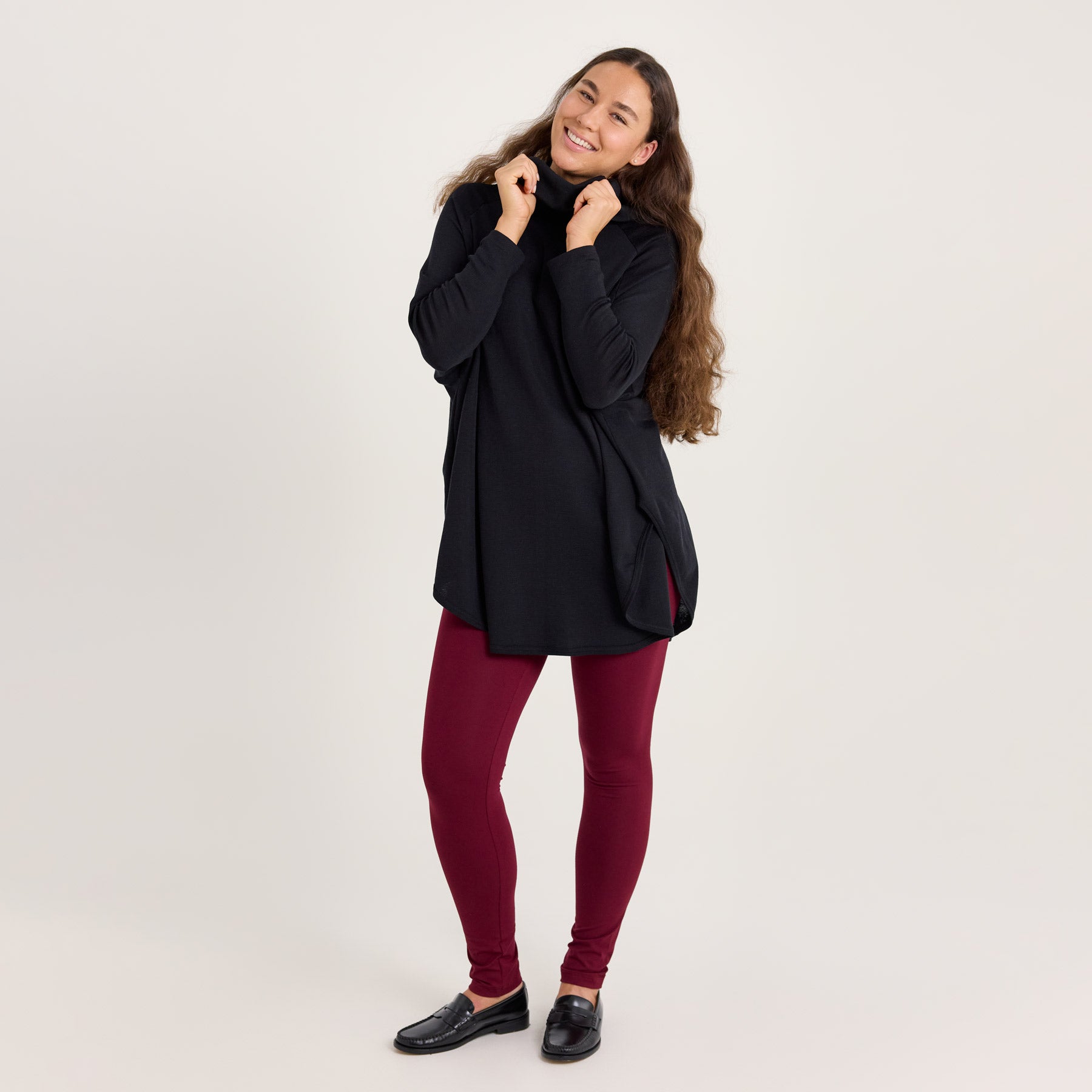 Mallilla on musta neuletunika, viininpunaiset bambuleggingsit ja mustat nahkakengät. Rento ja tyylikäs asu. Malli pitää käsillään kiinni neuletunikan kauluksesta, ja tuo esiin merinosilkin pehmeyden.