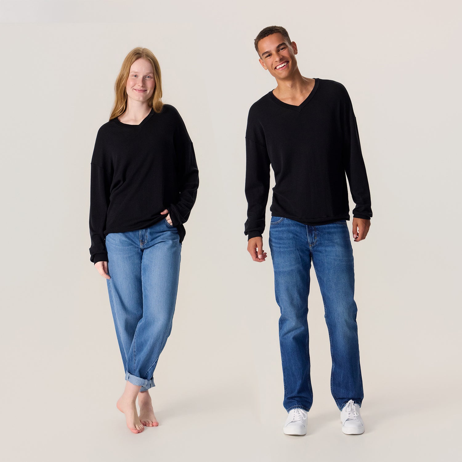 Mies ja nainen farkuissa ja unisex-mallisessa mustassa neulepaidassa. Neulepaidassa on v-pääntie ja pitkät hihat.