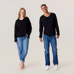 Mies ja nainen farkuissa ja unisex-mallisessa mustassa neulepaidassa. Neulepaidassa on v-pääntie ja pitkät hihat.